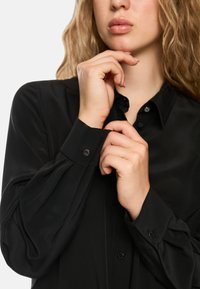 Schwarzes Langarmshirt aus glattem Stoff, mit klassischem Kragen und geknöpften Manschetten, die einen dezenten Glanz aufweisen.