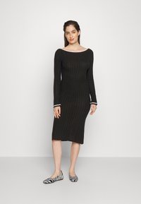 Μαύρο πλεκτό φόρεμα με ριμπ σχέδιο, μακριά μανίκια και λαιμόκοψη σε σχήμα βάρκας. Διαθέτει αντίθετη λευκή επένδυση στα μανίκια. Συνδυάζεται με παπούτσια σε μαύρο και άσπρο ρίγες.