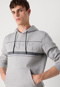 Gray hoodie with a subtle embossed "BOSS" logo, black drawstrings, and horizontal black accents across the chest. Kangaroo pocket design.
