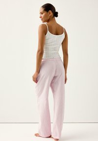 Canottiera bianca a coste con spalline sottili, abbinata a pantaloni a gamba larga a righe rosa chiaro con vita elasticizzata e orlo smerlato.