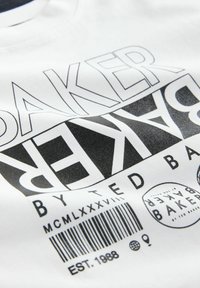 Camiseta de algodón blanca con texto negro en negrita, "BAKER", con tipografía variada y un gráfico de código de barras. Textura suave, ajuste casual.