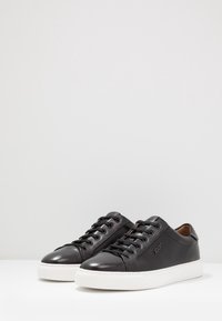 Baskets en cuir noir à finition lisse, semelle en caoutchouc blanche, bout rond et sept œillets pour les lacets. Logo embossé sur le côté.