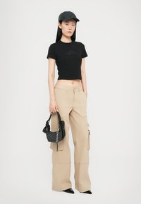 Black cropped t-shirt with a subtle logo, beige wide-leg cargo pants, black cap, and small black bag with mesh detailing and chain accents.