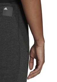 Graue Sporthosen verfügen über einen strukturierten Stoff, seitliche Eingrifftaschen und ein Adidas-Logo auf einem schwarzen quadratischen Patch nahe dem Bund.