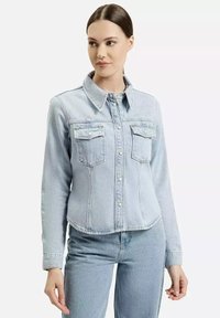 Jasnoniebieska dżinsowa kurtka z zapinaniem na guziki z przodu, dwoma kieszeniami na piersi, kołnierzem i długimi rękawami, o gładkiej fakturze i standardowym kroju.