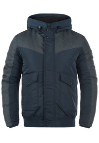 Tamno plava jakna s kapuljačom, punjena, s kontrastnom sivom tkaninom na ramenima i rukavima, koja sadrži produžene džepove na kopčanje.