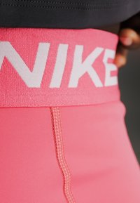 Κοντινό ενός ατόμου που φοράει ροζ κολάν Nike με φαρδύ λάστιχο μέσης που εμφανίζει το λογότυπο Nike με λευκά γράμματα.
