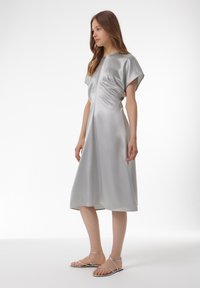 Zilveren satijnen midi-jurk met korte cape-mouwen en een vloeiende silhouet. Heeft een ronde halslijn en subtiele draperingsdetails.