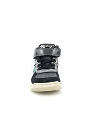Zapatilla negra y gris con una correa de velcro texturizada, cordones suaves, un cuello acolchado y una suela de goma blanca. Presenta un logotipo en la lengüeta.