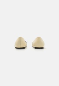 Scarpe piatte beige con una finitura in pelle liscia, punta appuntita, suola nera bassa e dettagli minimi, viste da dietro.