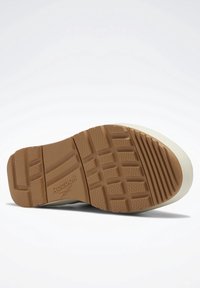 Sole tenisky Reebok s hnědým gumovým vzorem, bílým polstrováním a texturovaným povrchem pro lepší grip.