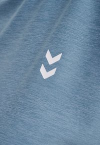 Lyseblå T-shirt i stof med en struktureret finish, med en hvid dobbelte chevron-logo nederst til højre.