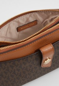 Brun læderhåndtaske med en tekstureret overflade og guldfarvede detaljer. Indvendigt har den en sandfarvet foring og et navneskilt med "MICHAEL KORS."