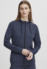 Jūras spēku krāsas zip-up kapuce, izgatavota no gludas auduma, ar priekšējo kabatu, regulējamiem saites un pieguļošu dizainu ar ribotām piedurknēm.