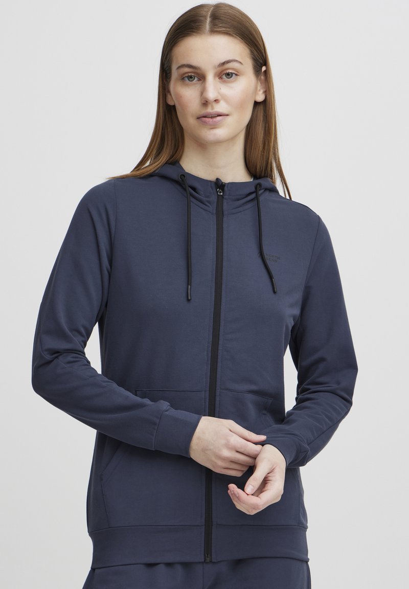 Jūras spēku krāsas zip-up kapuce, izgatavota no gludas auduma, ar priekšējo kabatu, regulējamiem saites un pieguļošu dizainu ar ribotām piedurknēm.