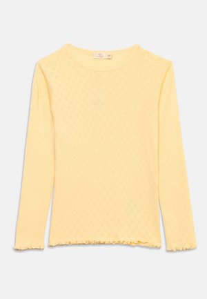 Gul langermet strikket topp med subtilt teksturmønster, rund halsutringning og volangkant på ermene og nederste kant.