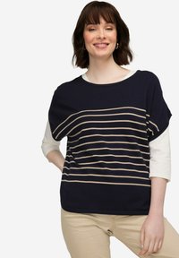 Námořnický modrý pruhovaný svetr s béžovými horizontálními pruhy, volný střih, kulatý výstřih a tříčtvrteční rukávy, vrstvený přes bílou košili.