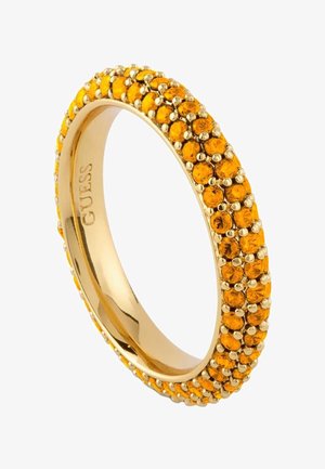 Złoty pierścionek z dwiema rzędami małych, okrągłych pomarańczowych kamieni osadzonych wokół obrączki, wewnętrzny grawerunek z napisem "GUESS".