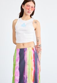 Hvit kort tanktopp med lyseblå logo, kombinert med et flerfarget stripete skjørt med grønne, rosa og lilla nyanser.