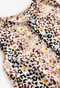 Leopardikuvioinen puuvillapusero, jossa on vaalea taustaväri, ruskeita ja mustia täpliä, keltaisia kukkia sekä valkoiset muovinapit pääntiellä.