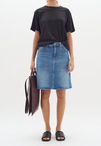 Svart bomullströja, blå denim A-linje kjol, svarta slip-on sandaler, och brun toteväska med slät textur. Enkelt, avslappnat klädset.