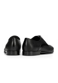 Scarpe in pelle nera con un design perforato, punta arrotondata e tacco basso. Un motivo testurizzato ricopre i lati e il retro per un ulteriore dettaglio.