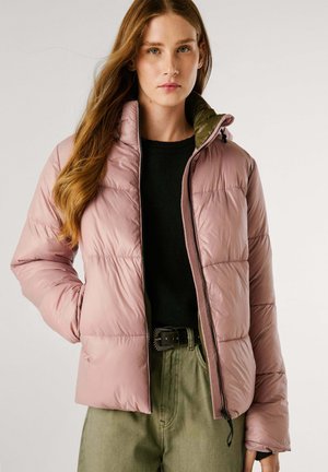 Rosa Pufferjacke mit gestepptem Design, Reißverschluss und olivgrünem Innenfutter. Getragen über einem schwarzen Pullover und olivgrünen Hosen.