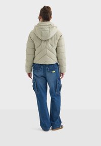 Chaqueta acolchada verde claro con capucha, diseño acolchado y corte cropped; combinada con vaqueros cargo azules holgados con bolsillos de carga.
