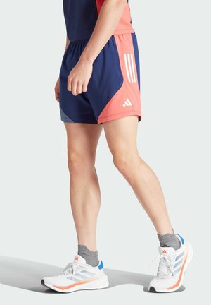 Pantalones cortos deportivos en azul y rosa con diseño de malla, que cuentan con tres franjas blancas y un acento lateral. Se combinan con zapatillas blancas y naranjas.