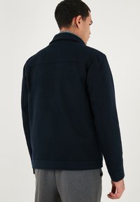 Námornícky kabát vyrobený z mäkkej tkaniny, s klasickým golierom a chrbtovým pásom, s minimalistickým dizajnom a strihom na mieru.