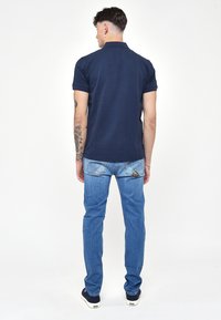 Námořnické polo tričko s krátkým rukávem, kombinované se světle modrými džínami. Džíny mají charakteristický design zadní kapsy a jsou tapered.