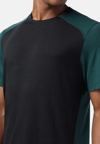 Svart kortärmad skjorta med texturerade gröna detaljer på axlarna, rundhalsad design och en slät tygfinish.