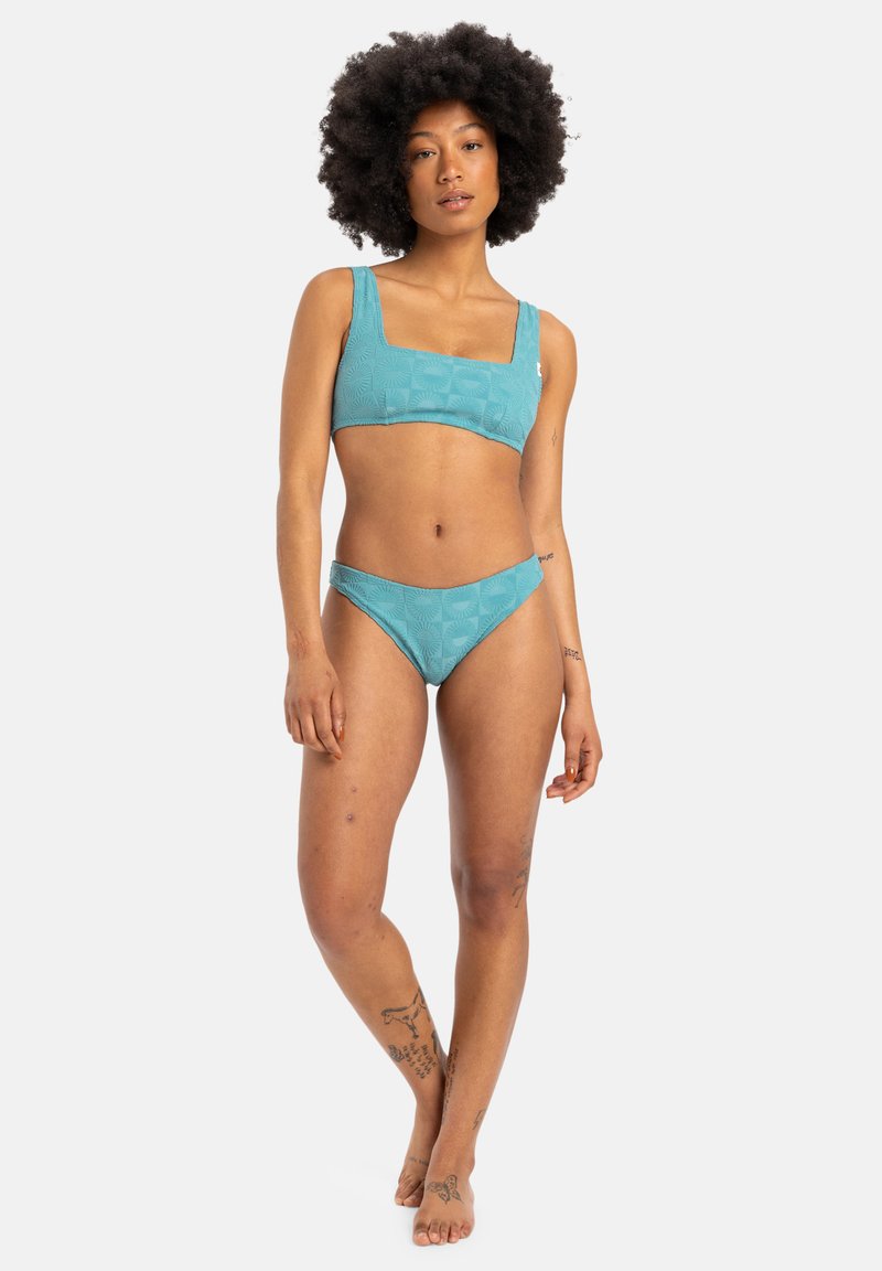 Tengere színű, textúrázott bikini szett, négyzet alakú dekoltázsú toppal és alacsony derékú alsó résszel, geometriai mintázattal az egész anyagon.