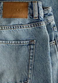 Ανοιχτό μπλε τζιν με ορατή πίσω τσέπη, θηλιά για ζώνη και καφέ δερμάτινο λογότυπο με την ένδειξη "JJXX" ραμμένο στη μέση.