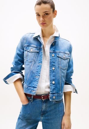 Lys blå denimjakke med knappelukking, brystlommer og oppbrettede ermer. Kombinert med en hvit skjorte og mørkerød belte.