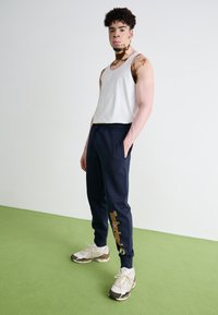 Námornícke tepláky s elastickým pásom majú na ľavom stehne žlté logo "Timberland"; skombinované s bielym tielkom a béžovými teniskami.