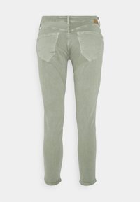 Vaqueros skinny verde claro con una textura suave, que cuentan con bolsillos traseros y una etiqueta de cuero marrón en la cintura. Diseño simple y funcional.