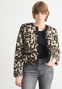 Luipaardprint nepbontjacket met zwarte accenten en knopen, lange mouwen en diepe zakken, gecombineerd met grijze jeans.