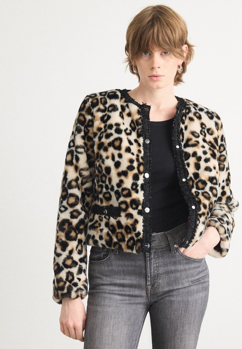 Luipaardprint nepbontjacket met zwarte accenten en knopen, lange mouwen en diepe zakken, gecombineerd met grijze jeans.
