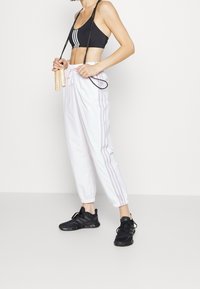 Svart sport-bh med tre vita ränder, vita joggingbyxor med grå ränder och svarta gympaskor. Hopprep hålls i händerna.