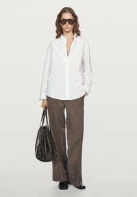 Camicia bianca a maniche lunghe, pantaloni marroni a righe sottili e borsa nera. Caratteristiche includono occhiali da sole oversize e una vestibilità comoda. Texture lisce.