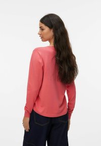 Sweat-shirt corail à manches longues en matière douce, doté d'un col rond, d'une coupe décontractée et de poignets côtelés. Porté avec un pantalon en denim foncé.