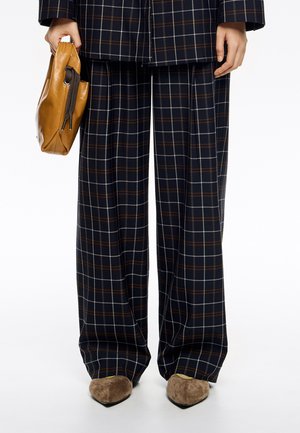 Pantalones anchos de cuadros azul marino con líneas blancas y marrones, combinados con un bolso de cuero marrón y zapatos de tacón alto beige.