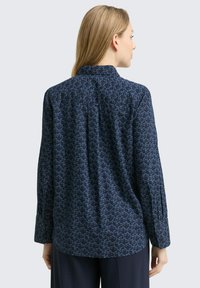 Marineblouse met een herhalend blauw bladpatroon, lange mouwen, knoopmanchetten en een kleine kraag. Zachte stof met een subtiele glans.