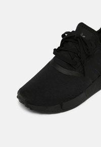 Czarne buty sportowe z siateczkową cholewką i gumową podeszwą. Sznurówki i trzy paski w kolorze czarnym akcentują design. Okrągły czubek z teksturowanymi detalami.
