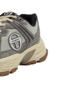 Graue Sportartike mit einem Netzobermaterial, Wildlederakzenten, einer Gummisohle und einem kreisförmigen Logo an der Seite. Die Schnürsenkel sind cremefarbig.