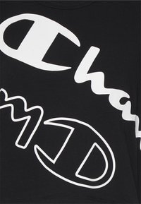 Czarna koszulka z dużym białym napisem i logo. Miękki, elastyczny materiał z klasycznym okrągłym dekoltem. Brak dodatkowych wzorów lub akcentów.