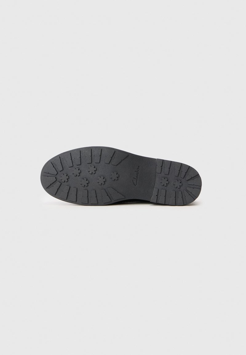 Suela de zapato de goma negra con un patrón de banda de rodadura perforado, que presenta múltiples secciones elevadas para tracción y durabilidad.