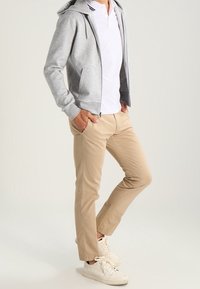 Grå zip-up hoodie över en vit polo, parat med beige byxor och vita sneakers. Har en avslappnad design och lös passform.