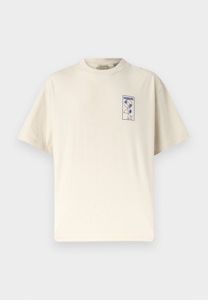 Trumpa kreminės spalvos marškinėlių su mėlynu mažuoju Snoopy, kuris laiko įrašą, ir užrašu „peanuts“ viršutinėje kairėje krūtinės pusėje.